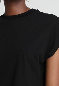 Svart kortärmad t-shirt med rund hals och mjukt bomullstyg. Ärmarna har en lätt rullad design.