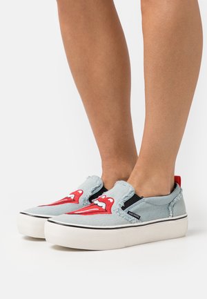 Baskets slip-on bleu clair avec un graphisme de lèvres rouges, bords effilochés, panneaux latéraux élastiques et semelles en caoutchouc blanches. Logo visible sur le côté.