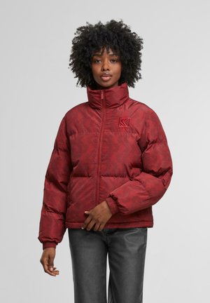 Rote Pufferjacke mit hohem Kragen und Reißverschluss, ausgestattet mit einem geometrischen Muster und gerippten Bündchen. Logo auf der linken Brust.