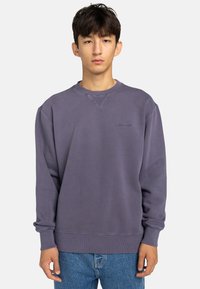Purple sweatshirt with ribbed crewneck, dropped shoulders, and elastic cuffs. Features a subtle logo on the chest and smooth texture.