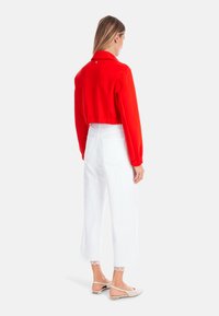 Red cropped jacket with a collar, elastic waistband, paired with white wide-leg pants featuring lace trim at the hem and beige flats.