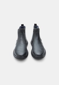 Botas negras de cuero hasta el tobillo con textura suave, punta redonda, cremalleras laterales y tiradores en la parte posterior para facilitar su uso.