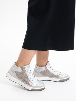 Person wearing mid-top sneakers with white soles, silver accents, and textured panels, paired with black cropped pants.