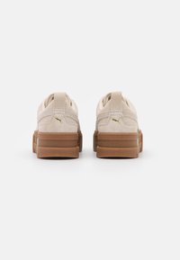 Baskets en daim beige avec une semelle en caoutchouc, présentant une semelle intermédiaire texturée et un accent logo doré au niveau du talon. Design minimaliste.