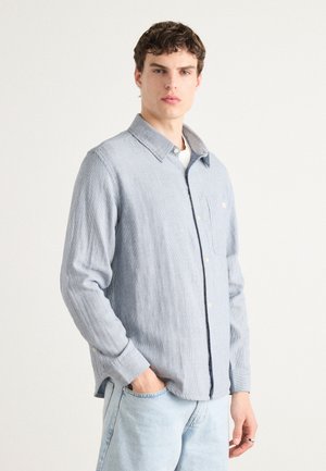 Light blue, long-sleeve button-up shirt with a textured fabric, pointed collar, single chest pocket, and contrasting collar detail.