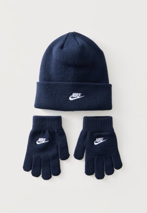 Set di berretto lavorato a maglia blu navy e guanti con loghi Nike bianchi su ogni articolo, disposti su uno sfondo chiaro.