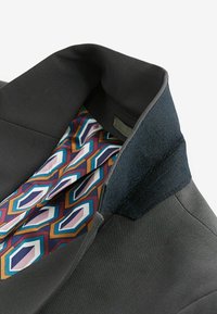 Sort blazerkrave med kontrasterende tekstureret mørk stof. Foret med et geometrics mønster i lilla, blå og brune nuancer.