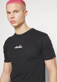 Black cotton t-shirt with short sleeves, featuring white "ellesse" logo on chest, and a small logo accent on sleeve.
