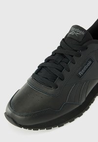 Zwarte leren sneaker met een gestructureerd oppervlak, voorzien van een gewatteerde kraag, tonale veters en een rubberen zool. Reebok-logo op de zijkant.