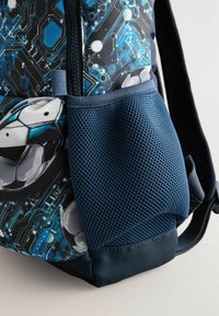 Nahrbtnik z motivom nogometne žoge in modro-črnim oblikovanjem, ki spominja na cirkuit. Teksturna modra mrežasta stranska žepka dodaja funkcionalnost. Zipper zapiranje.