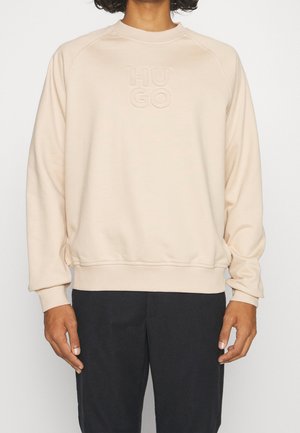 Sweatshirt beige clair avec un col ras du cou et des manches raglan, arborant un logo "HUGO" en relief sur le devant. Texture douce et coupe décontractée.