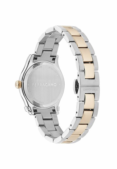 Ferragamo rozsdamentes acél karóra ezüst és arany színű láncszemes szíjjal, látható hátlappal, amelyen a márka gravírozása és arany színű korona található, fehér háttéren.
