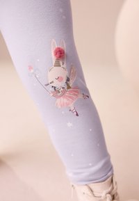 Svetlofialové legíny s kresleným králikom v ružovom tutu, zdobené detailom s brmbolcom a hviezdami, vyrobené z elastickej bavlnenej látky.
