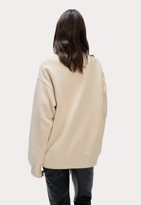 Felpa beige oversize con collo a giro e spalle scese. Tessuto morbido con polsini a costine, abbinata a pantaloni in pelle neri.