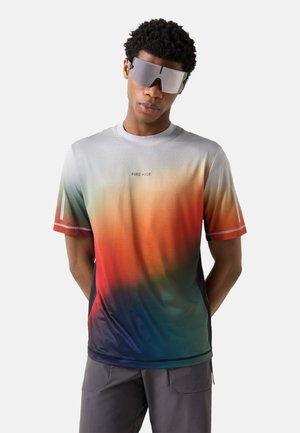 Mann trägt ein kurzärmeliges Hemd mit Farbverlauf und „FIRE+ICE“-Logo sowie große reflektierende Sonnenbrille, steht mit den Händen hinter dem Rücken.