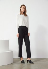 Suéter blanco de punto con cuello barco, combinado con pantalones negros de corte ajustado y tacones negros tipo slingback. Texturas suaves y diseño minimalista.