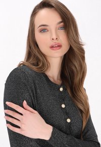Top nero luccicante con scollatura rotonda e tre bottoni color crema. Il tessuto ha una consistenza morbida e una leggera lucentezza.