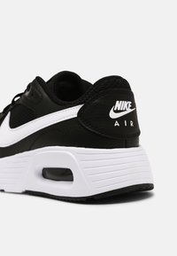 Musta lenkkari, jossa on teksturoitu nahka ja verkko-osat. Varustettu valkoisella swoosh-logolla ja ilmatyynyllä pohjassa, valkoisilla uritettujen yksityiskohtien kanssa.