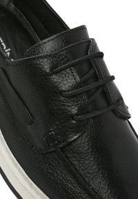 Scarpa in pelle nera con superficie texturizzata, sei fori per i lacci e suola in gomma bianca con un sottile motivo a scanalature.