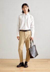 Lightweight white button-up shirt, beige trousers, black belt, black leather tote bag, and dark shoes. Simple design, neutral colors.