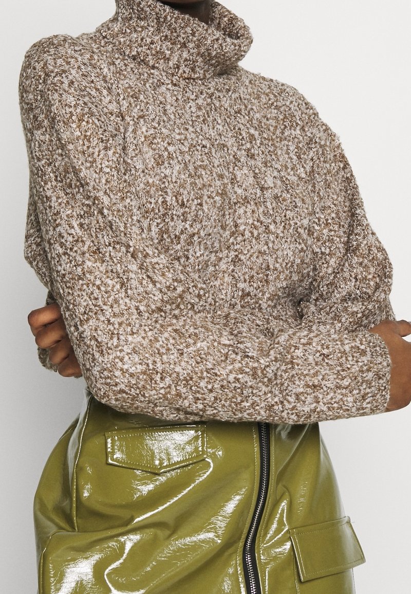 Maglione a collo alto in maglia grossa nei toni del marrone e della crema, con una vestibilità rilassata e un tessuto textured. Abbinato a una gonna verde lucida.