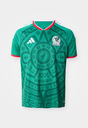 Zelena mehiška nogometna majica z rdečo in belo obrobo, vzorec azteškega koledarja, logotip Adidas in grb mehiške ekipe spredaj.