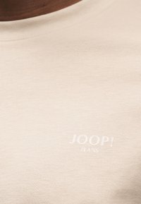 Μπεζ βαμβακερό t-shirt με στρογγυλή λαιμόκοψη και λεπτή υφή, με το όνομα της μάρκας "JOOP!" τυπωμένο σε λευκό στο στήθος.
