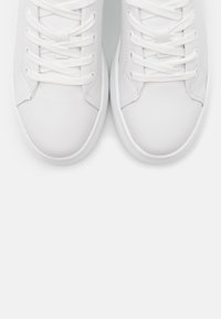 Baskets en cuir blanc avec une texture lisse, présentant un bout rond, des lacets plats et un design simple. Accentuées par une semelle en caoutchouc texturée.
