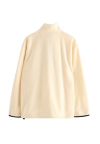 Krémově zbarvená fleecová bunda s dlouhými rukávy, vysokým límcem a černým lemováním viditelným na manžetách a spodním okraji.