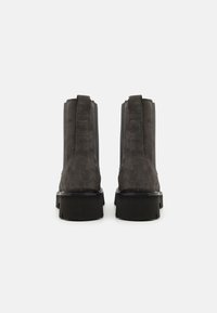 Bottes chelsea noires en suede avec une semelle épaisse, des panneaux latéraux élastiques et des boucles à l'arrière, présentant une texture lisse et un design minimaliste.
