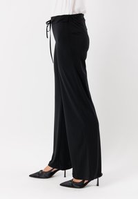 Pantaloni neri a gamba larga con vita regolabile, tessuto morbido e vestibilità rilassata. Abbinati a décolleté nere a punta.