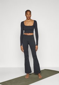 Čierny crop top s dlhým rukávom a štvorcovým výstrihom, kombinovaný s čiernymi širokými nohavicami s vysokým pásom. Hladká textúra, minimalistické značkovanie, priliehavý strih.