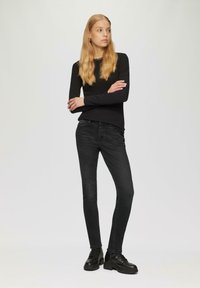 Zwarte top met lange mouwen en donkere skinny jeans, gecombineerd met zwarte enkellaarsjes. Eenvoudig ontwerp, aansluitende vorm en soepele textuur.