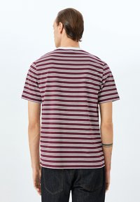 Camiseta de rayas marrón y blanca con cuello redondo, mangas cortas y dobladillo recto. Textura suave, llevada con jeans oscuros.