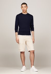 Haut en maille à manches longues navy associé à un short cargo beige avec des poches latérales, complété par des baskets blanches. Design épuré et minimal.