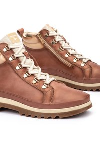 Botas de senderismo de cuero marrón con un acabado texturizado, que presentan herrajes dorados, cordones color crema y un diseño de caña alta con cremallera lateral. Suela ligera.