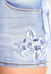 Jeansshorts i ljusblått med blommig brodyrdesign i lila, med klassisk passform och medelhög midja, samt synliga sömnadsdetaljer.