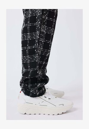 Black and white checkered pants tucked into white athletic sneakers with thick soles and minimal black detailing.