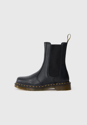 Botte Chelsea en cuir noir avec panneaux latéraux élastiques, surpiqûres jaunes sur la semelle et languette de tirage marron à l'arrière.