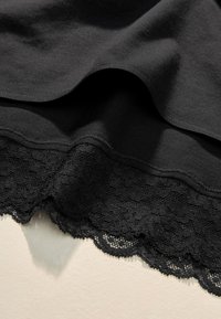 Fekete pamutanyag sima felülettel, az alján hullámos csipke szegéllyel, amely részletgazdagságot ad az aljának.
