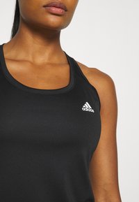 Czarny sportowy top na ramiączkach z okrągłym dekoltem, cienkimi paskami i białym logo Adidas po lewej stronie. Gładki, elastyczny materiał.
