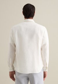 Camicia bianca in lino con maniche lunghe, orlo dritto e polsini con bottoni. Il retro presenta cuciture sottili e un colletto standard.