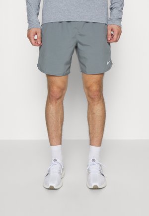 Shorts Nike gris en matériau léger, avec une coupe décontractée et des fentes sur les côtés, associés à des chaussures de sport blanches et des chaussettes.