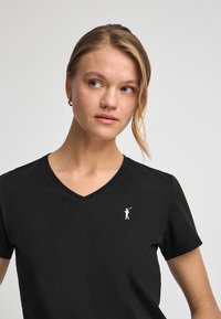 Czarna bawełniana koszulka z dekoltem w serek. Zawiera małe białe logo golfisty na lewej piersi. Teksturowana tkanina i krótkie rękawy.