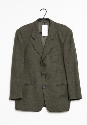 Dunkelgrüner Fischgrät-Wollblazer mit drei Knöpfen, Revers mit Kerbe, Pattentaschen und einem weißen Etikett an einem schwarzen Bügel.