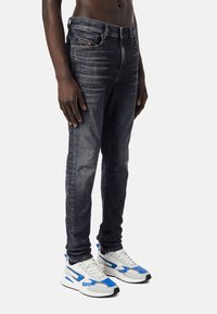 Mörk tvättade jeans i slim fit med subtila slitningar, fem fickor och bälteshällor; matchade med vita och blå sneakers.