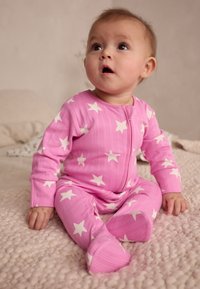 Body rose côtelé avec motif d'étoiles blanches, manches longues et fermeture éclair à l'avant. Bébé assis sur une couverture texturée.