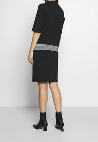 Vestido negro con mangas cortas, con una cintura a rayas blanca y negra. Combinado con botas negras hasta el tobillo, de tela suave, diseño hasta la rodilla.