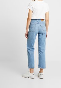 Vaqueros de denim azul claro con corte recto, que cuentan con dos bolsillos traseros, una etiqueta de cuero y un dobladillo deshilachado. Combinados con zapatillas blancas.