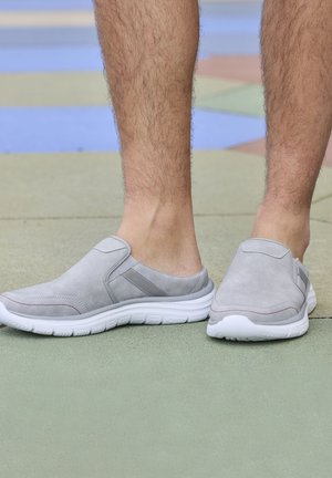 Gray slip-on shoes with suede texture, white rubber soles, and subtle red accents. The design features elastic side panels for easy wear.